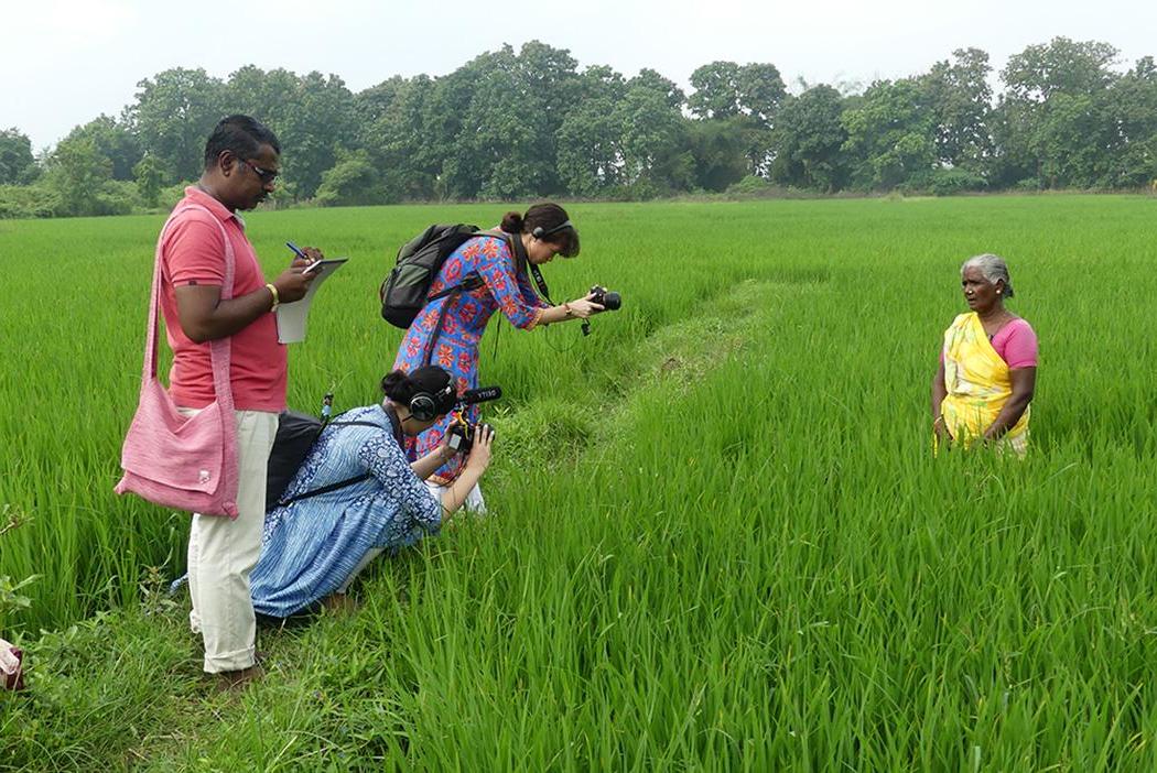 Three people filming a women in a green field